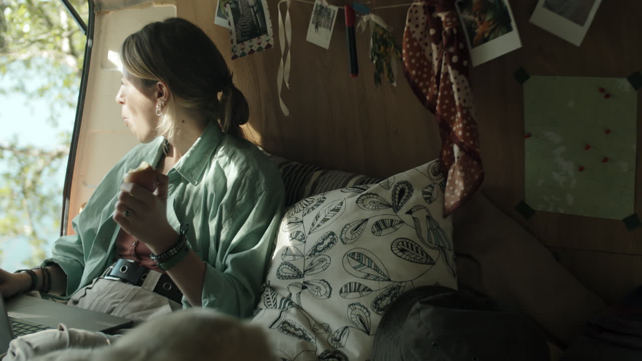 노트북 을 사용 하고 여행 트레일러 에서 사과를 먹고 있는 여자