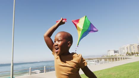 video de un feliz niño afroamericano divirtiéndose con una cometa, corriendo por la playa