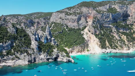 los barcos turísticos disfrutan de las vacaciones de verano en la playa de cala goloritze y la formación rocosa en cerdeña, italia - círculos aéreos de 4k