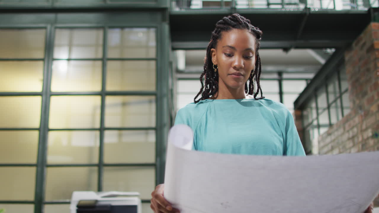 Happy african american female architect looking at architectural blueprints at office
