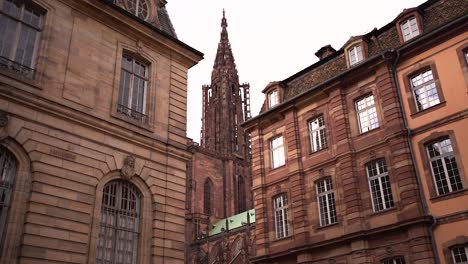 Strasbourg-Notre-Dame-Cathedral-tower-view-through-typical-buildings-on-cloudy-day,-France