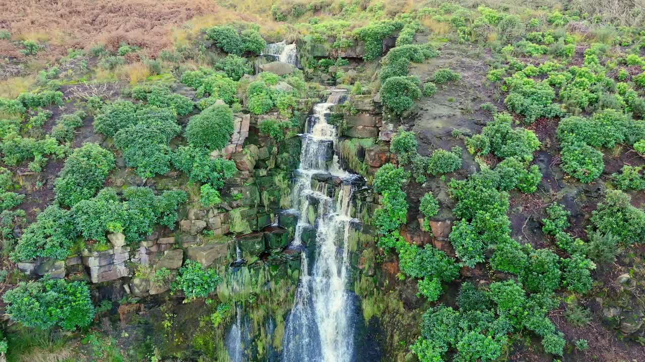 Yorkshire moor's beautiful waterfall, aerial perspective: water surges over substantial rocks, falling into a deep blue pool, hikers below
