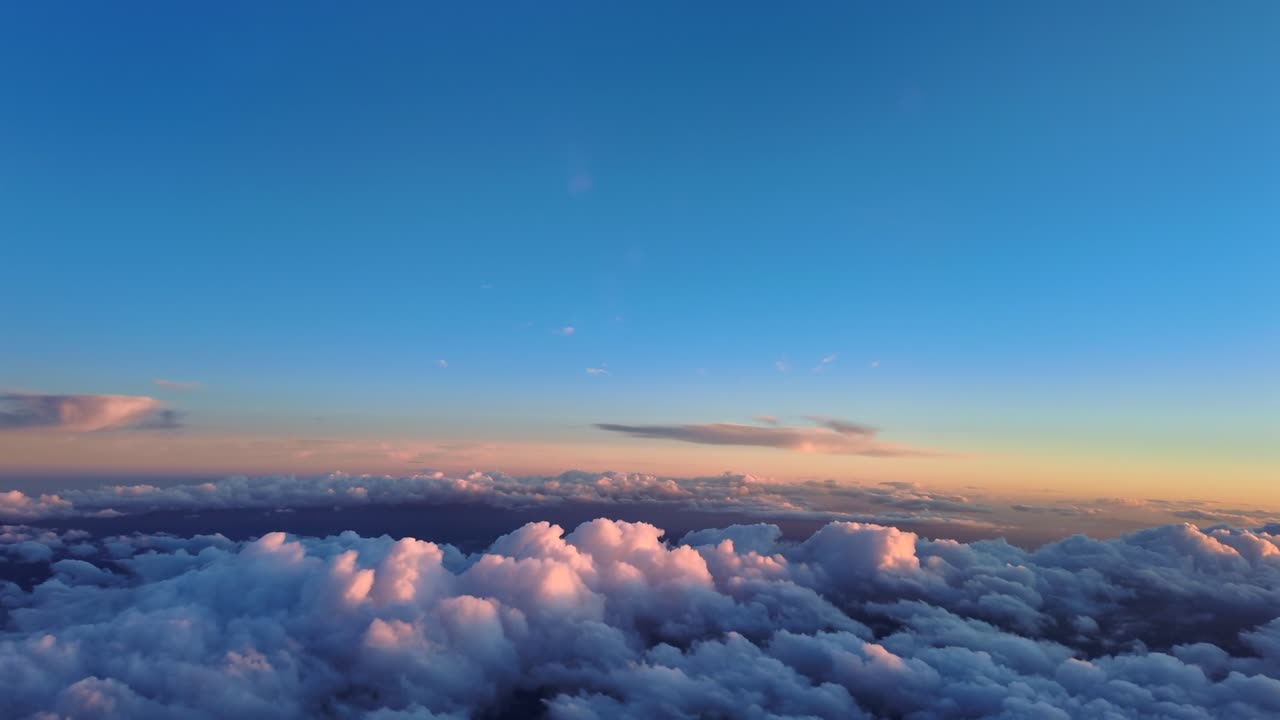 Vista dagli occhi del pilota mentre si sorvola nuvole cotonose illuminate dalla luce soffusa del tramonto. Scena catturata dalla cabina di pilotaggio di un aereo a reazione.