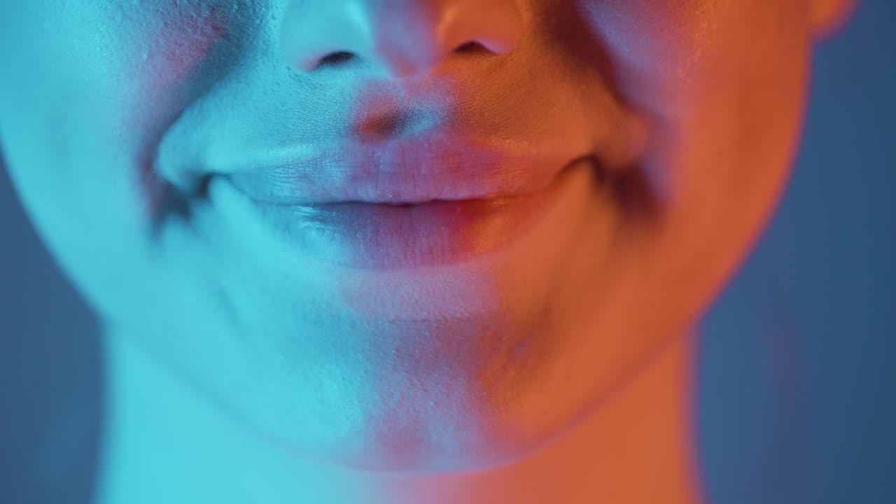 Extreme close up shot of a beautiful woman lip while she smiles into the camera with beautiful white teeth and radiates joy with turquoise orange contrast in her face