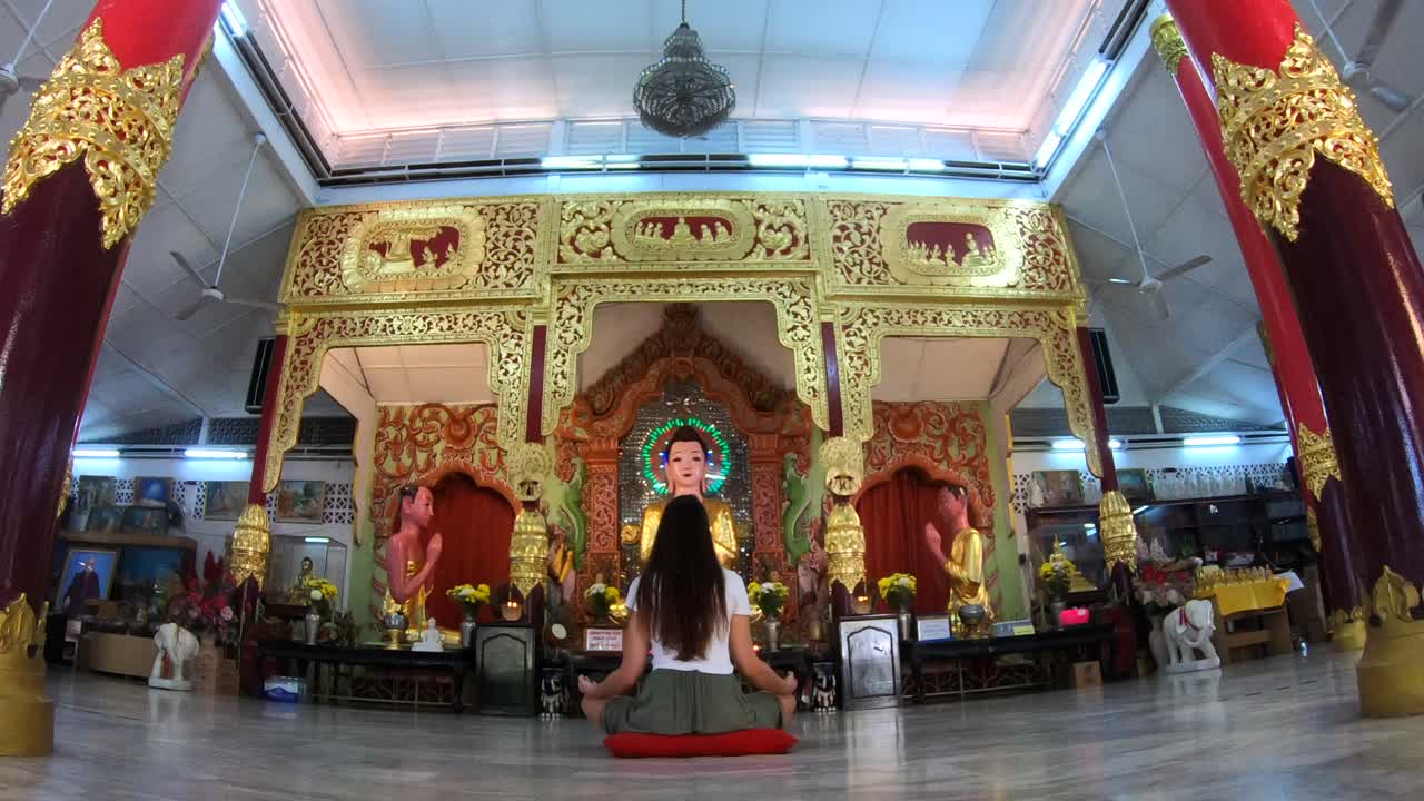 Woman meditating in a buddhist temple on her cultural travel through Asia, seeking God and Peace