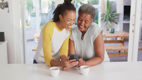 Madre-E-Hija-Afroamericana-Sonriendo-Mientras-Usan-Un-Teléfono-Inteligente-Juntos-En-Casa