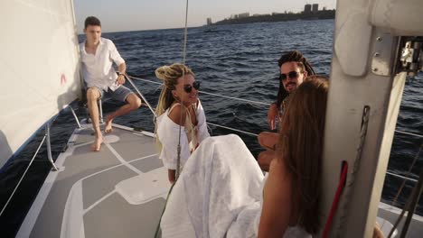 A-company-of-young-happy-friends-sail-on-a-yacht-bow-on-a-summer-day,-friends-share-interesting-stories-about-their-life-style-with-each-other,-men-and-women-relax-in-the-sun.-High-angle-view-from-the-sail