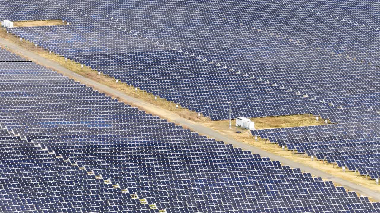 Drone camera smoothly pans across expansive photovoltaic solar panels under bright natural daylight