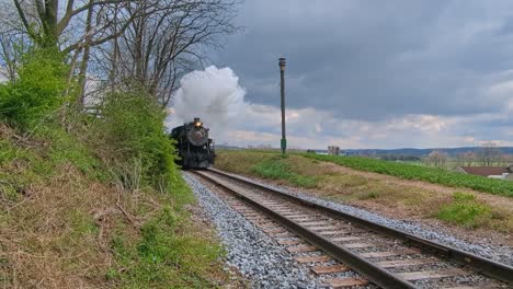 una vista de un antiguo tren de pasajeros de vapor restaurado que se acerca soplando vapor en un día de primavera