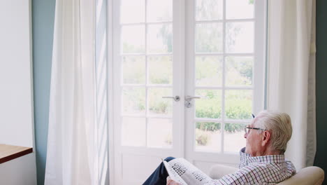 senior man sitting in an armchair doing crossword