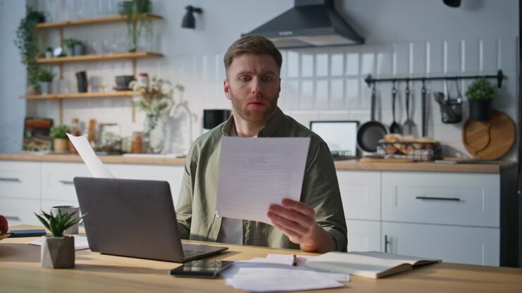 Focused professional reading paper at home office. Bearded freelancer analyzing
