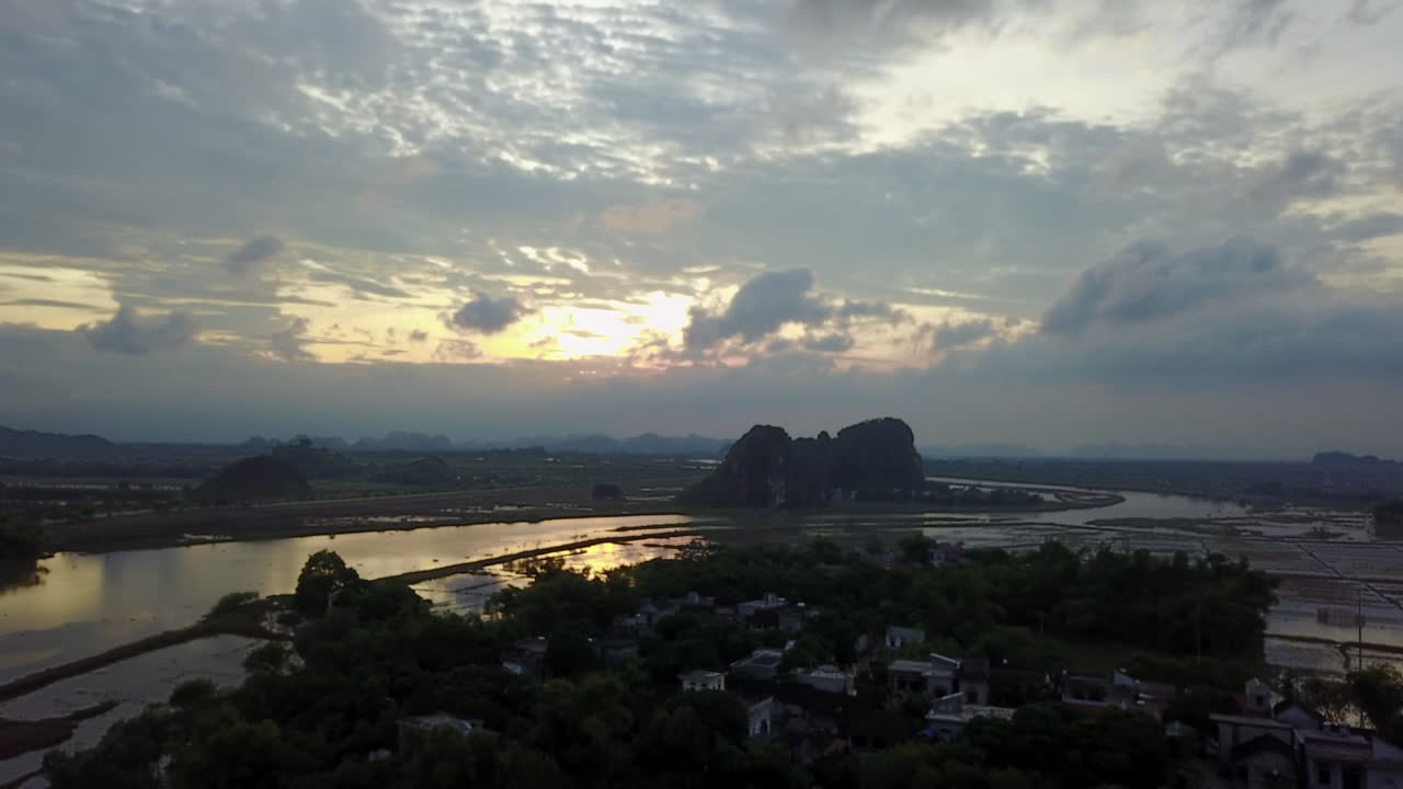 Experience a mesmerizing frontal tracking shot of the Day River and flooded rice plantation areas in Ninh Binh, Vietnam, during a beautiful sunset. Witness the golden light reflecting on the water.