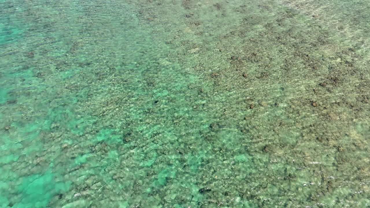 Aerial footage captures clear, shallow waters over a rocky beach in Phuket, Thailand, showcasing vibrant turquoise hues and natural textures