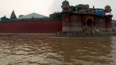 Cinematic-Ancient-Holy-city-Varanasi-India-Ganges-River-canal-boat-cruise-Northern-State-people-on-steps-Ghat-Pradesh-Province-landscape-gray-cloudy-fire-smoke-right-follow-motion