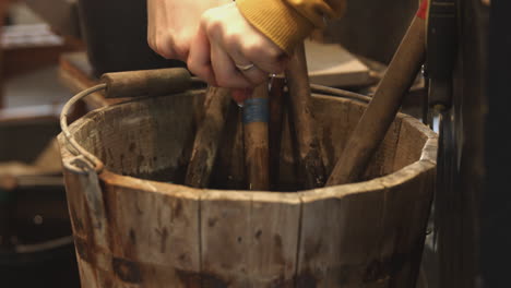 a rag is dipped and the water in a wood bucket filled with tools and then wrung out