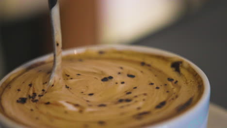 slow motion close-up shot of a spoon stirring a fresh cup of poured cappuccino