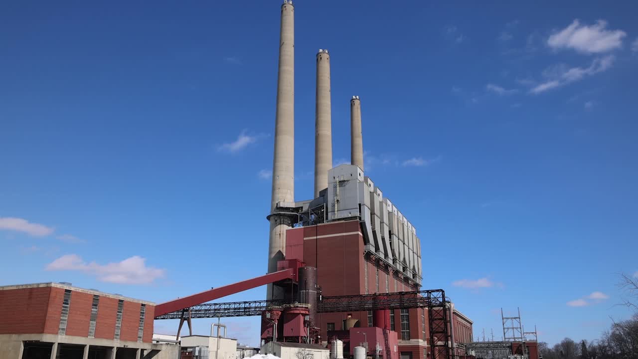 Coal burning power plant with three smoke stacks tilting down to river.