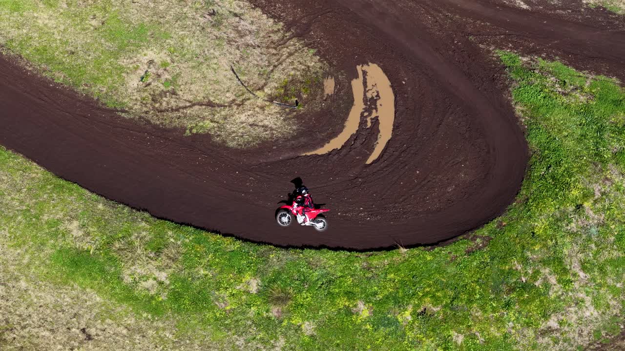 Motocross rider navigates sharp dirt track curve, aerial perspective, bright daylight, dynamic movement