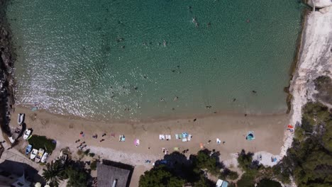 Vista-Aérea-De-Pájaro-De-La-Bahía-De-Porat-En-La-Isla-De-Bisevo,-Croacia-Con-Gente-Nadando-En-Aguas-Transparentes-De-La-Playa-De-Arena