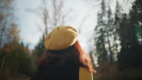 elegant lady wearing yellow beret and sunglasses enjoys nature scenic view with trees in background, sunlight creates soft glow as she gazes upward, appreciating beauty of autumn