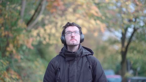 Un-Hombre-Europeo-Con-Estilo,-Con-Barba-Y-Gafas,-Pasea-Tranquilamente-Por-Los-Suburbios-Otoñales-De-Munich,-Profundamente-Inmerso-En-Las-Melodías-De-Sus-Auriculares,-Absorbiendo-La-Tranquilidad-Estacional.