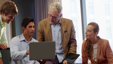 Businessman-and-coworkers-discussing-over-laptop-at-desk