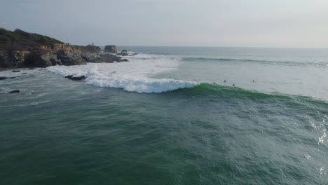 aerial rotating shot of a wave rolling through with surfers waiting for the next one