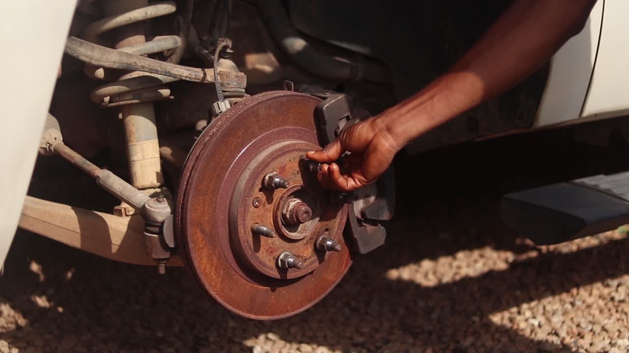A hand places a lug nut on the car's wheel rotor and tightens it with a cross wrench