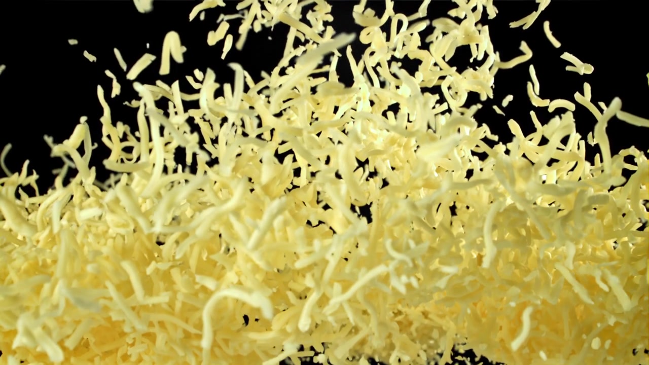 Formaggio grattugiato che cade al rallentatore su sfondo nero.