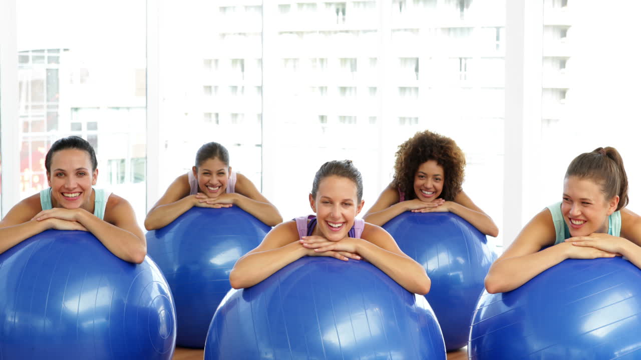 Fitness class in studio leaning on exercise balls smiling at camera