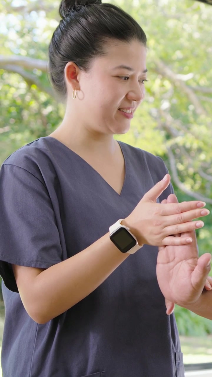 Video verticale: Paziente che offre la mano, terapista in camice che palpa il polso vicino a una finestra, controllando il movimento