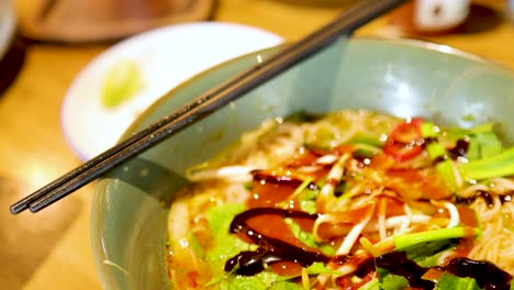 A close-up of sauce being drizzled over a vibrant bowl of Vietnamese pho, highlighting fresh ingredients and rich colors under warm lighting