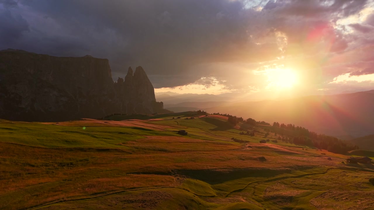 Sunset over Sciliar above Alpe di Siusi in the Dolomites, with golden alpine meadows, dramatic clouds and warm light creating a scenic mountain landscape.