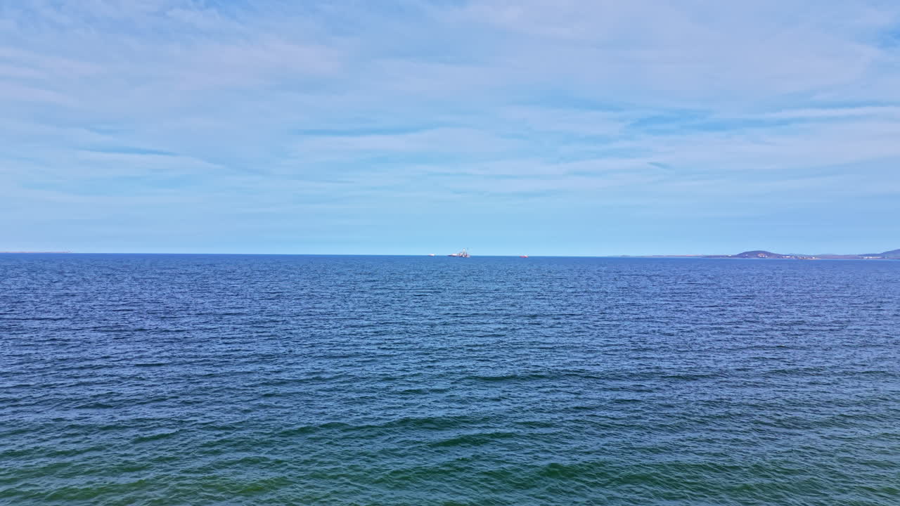 Rolig havudsigt med skib i det fjerne under blå himmel på en solrig dag, der fremhæver havets vidde og horisontlinjen.