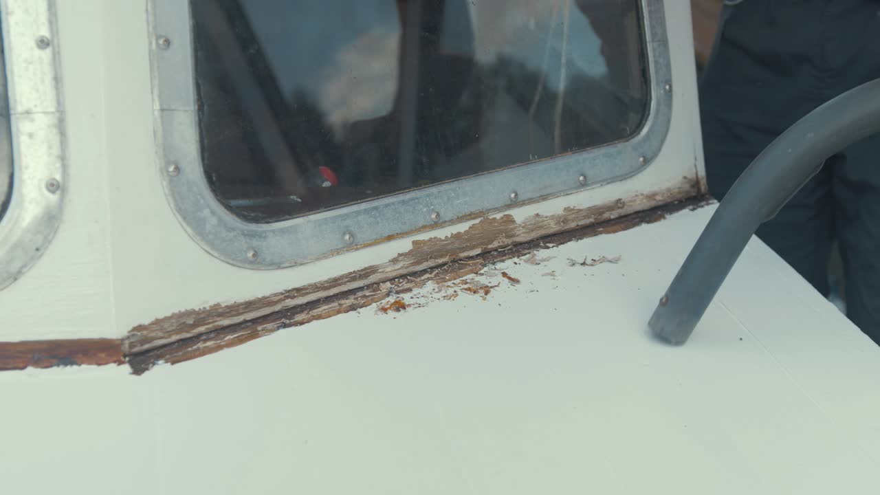 목수는 나무 파편을 후버링하여 나무 보트 앞 유리를 수리합니다.