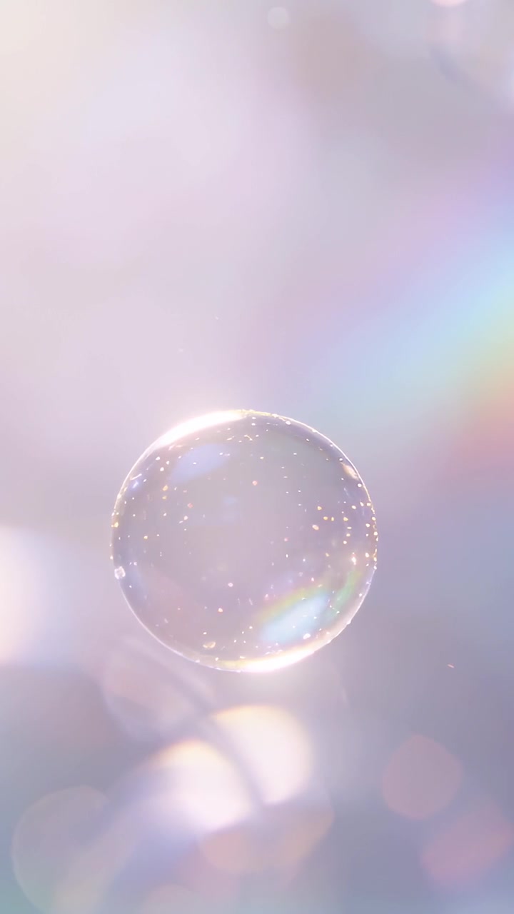 Video verticale: Una bolla di sapone principale che si muove dolcemente nell'aria, ruotando verso il basso in studio con bokeh pastello.