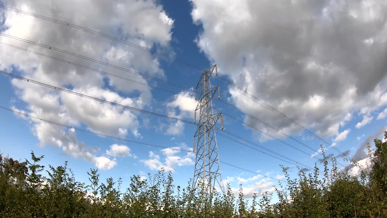 Time-Lapse of a National Grid electricity power pylon in a rural location with blue sky and wind clouds passing by, England, UK