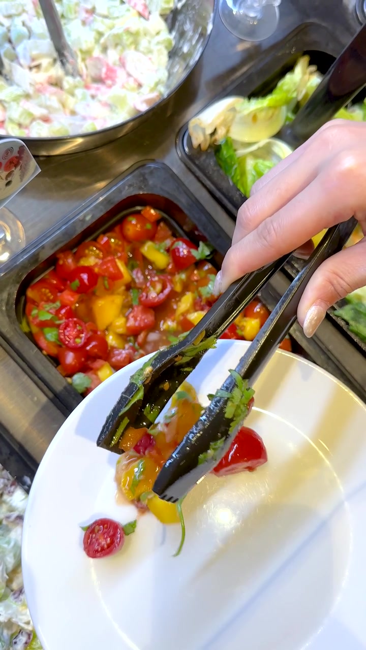 A person uses black tongs to serve fresh cherry tomato salad onto a white plate