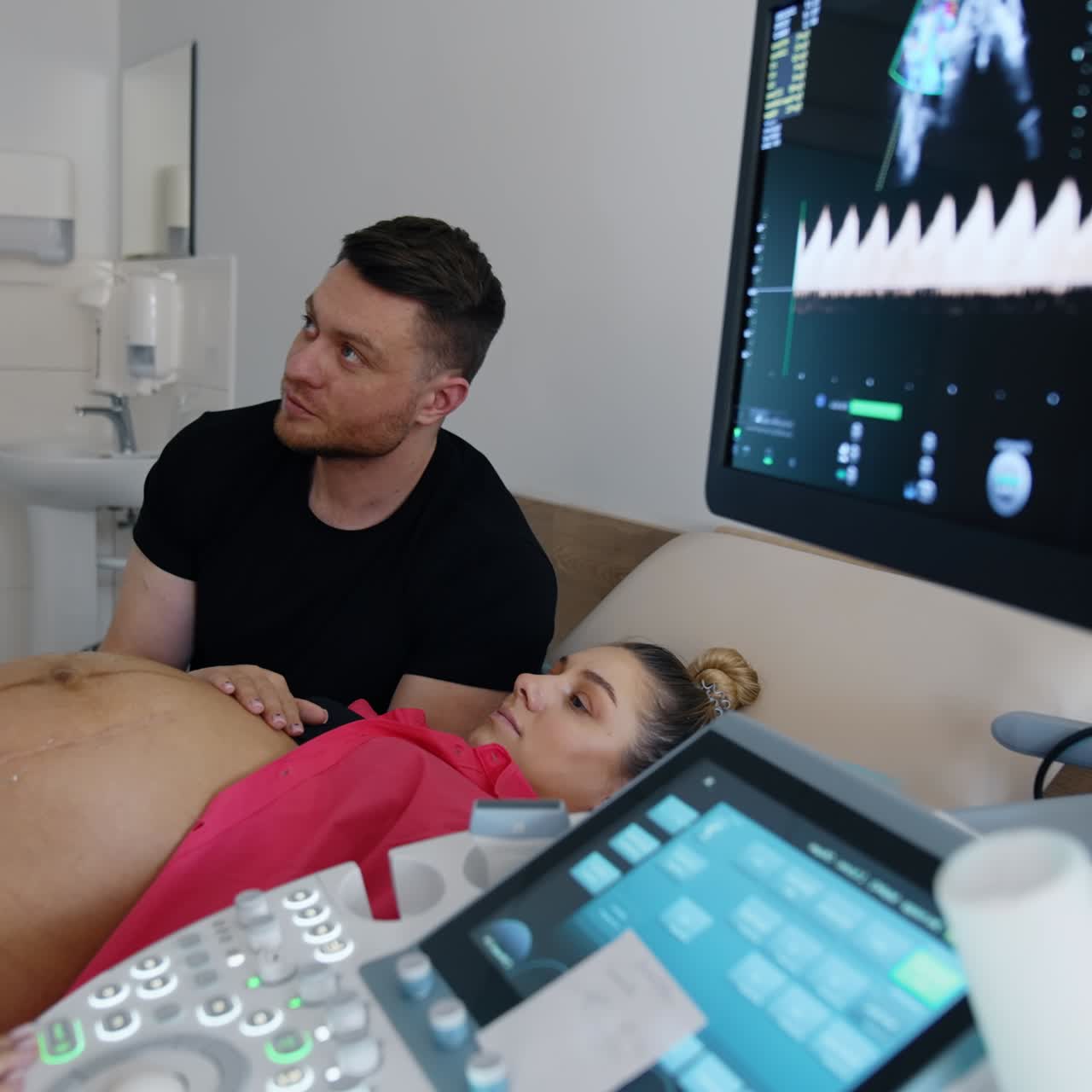 Un'ostetrica controlla la donna incinta con apparecchiature a ultrasuoni. I futuri genitori guardano attentamente il monitor.