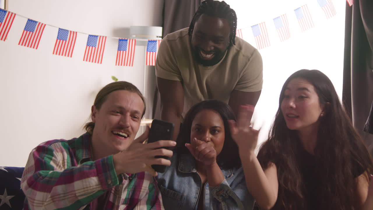 друзья дома празднуют с партией день независимости америки 4 июля, делая видео звонок на мобильный телефон.