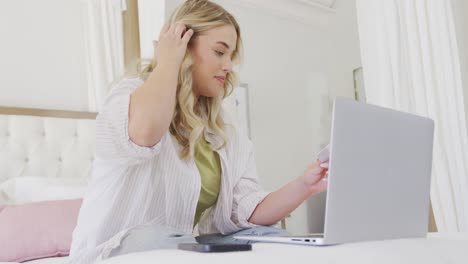 mujer caucásica feliz de talla grande usando una computadora portátil y sosteniendo una tarjeta de crédito en cámara lenta