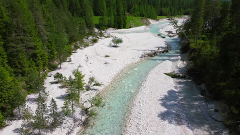 pristine-natural-environment-with-crystal-clear-turquoise-stream-surrounded-by-white-rocks-on-river-banks-and-lush-greenery-on-summer-day