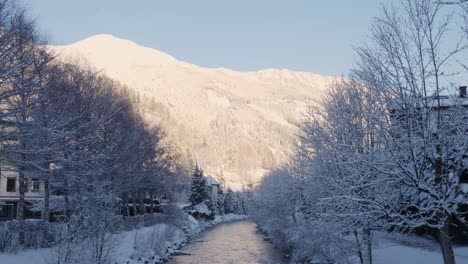 stream flowing calmly surrounded by snow laden mountains and snow covered trees during extreme winters