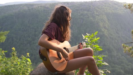 young woman playing acoustic guitar on mountaintop