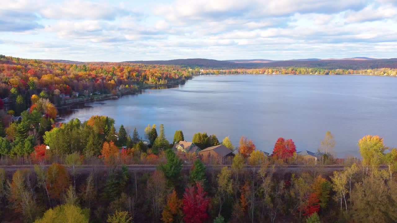Aerial establishing shot of a lake surrounded by vibrant forest in Estrie, Quebec