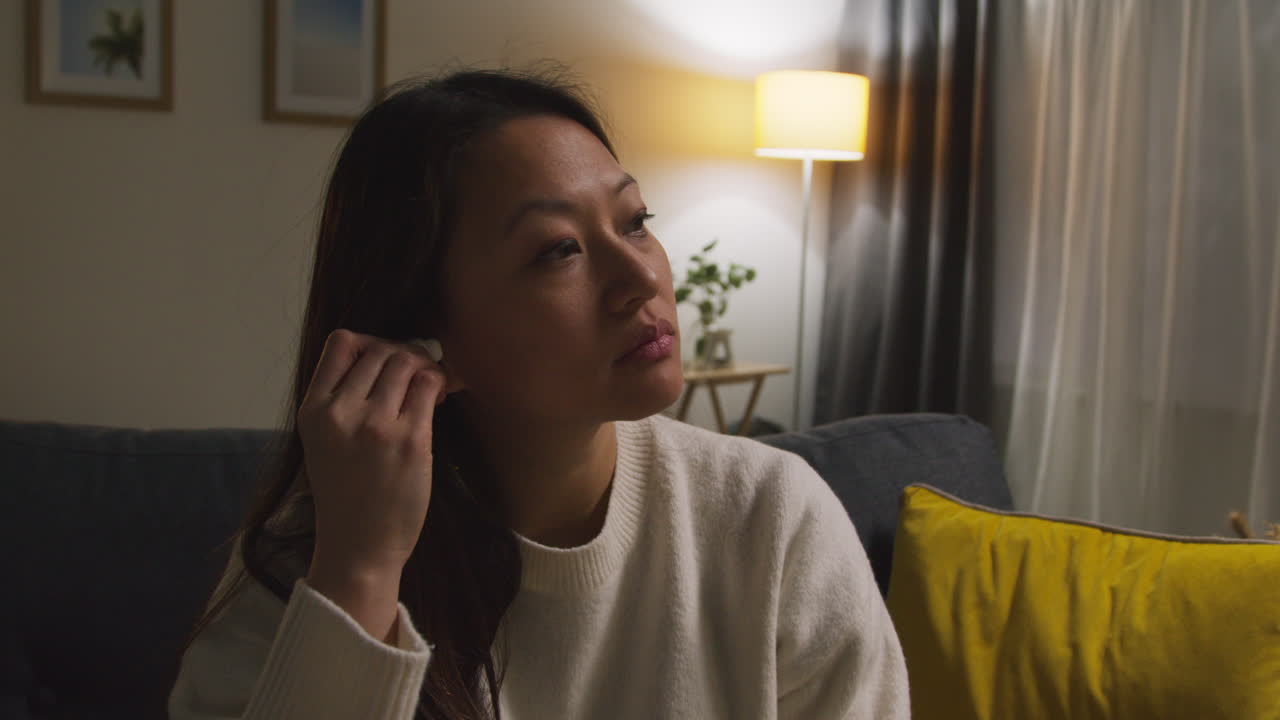 mujer pasando la noche en casa en el sofá poniendo auriculares inalámbricos y transmitiendo música o podcast desde el teléfono móvil