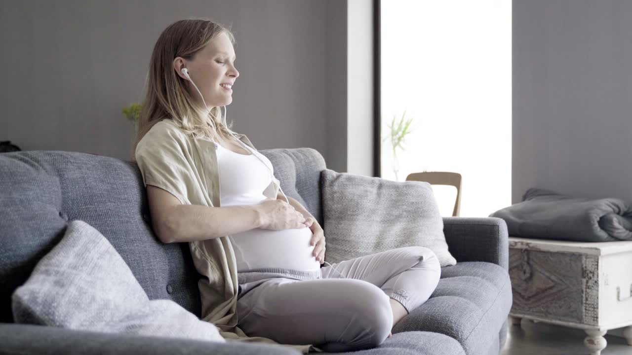 행복한 임신한 여성이 음악을 즐기고 배를 만지고 있습니다.