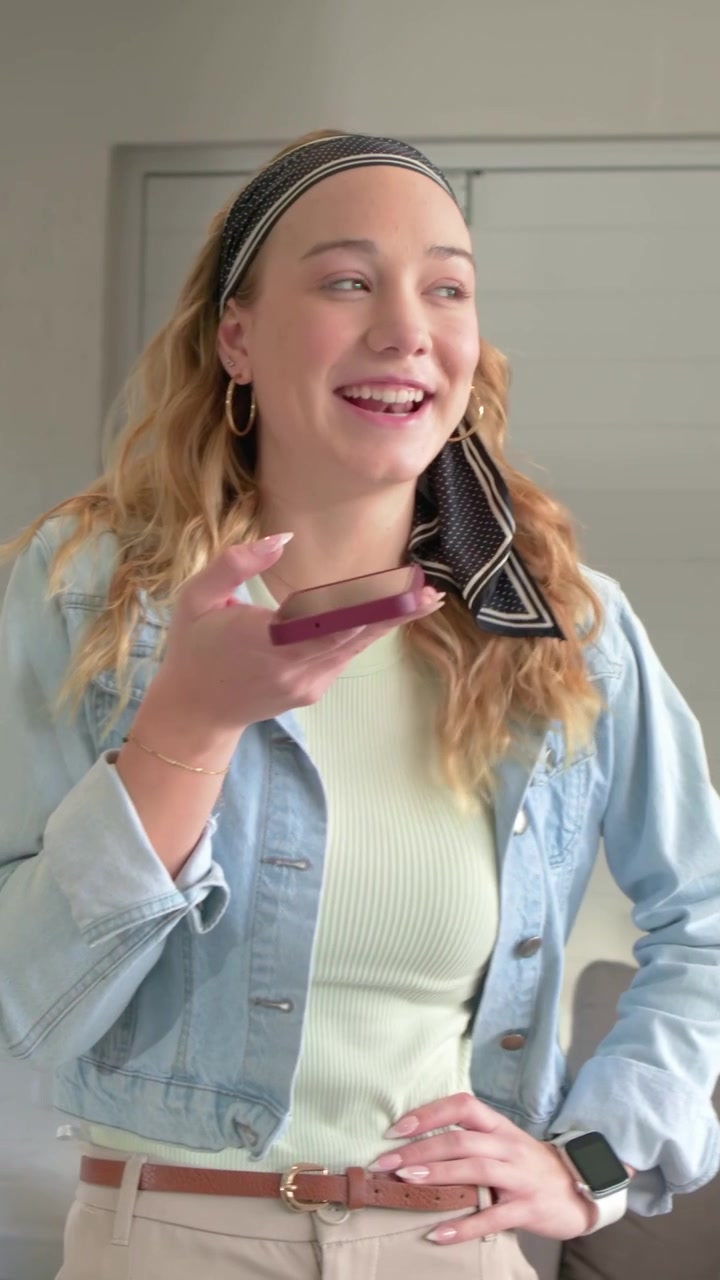Video verticale: Donna in jeans che tiene un telefono con custodia viola alla bocca, parla al telefono e sorride a casa.
