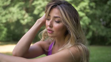 primer plano, vista en cámara lenta de una mujer rubia sentada en un parque estirándose antes de hacer ejercicio