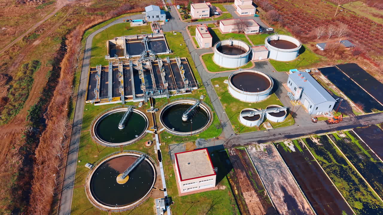Comprehensive aerial shot of sewage treatment plant and surrounding fields. View of industrial water tanks, aeration basins, and agricultural landscape in background